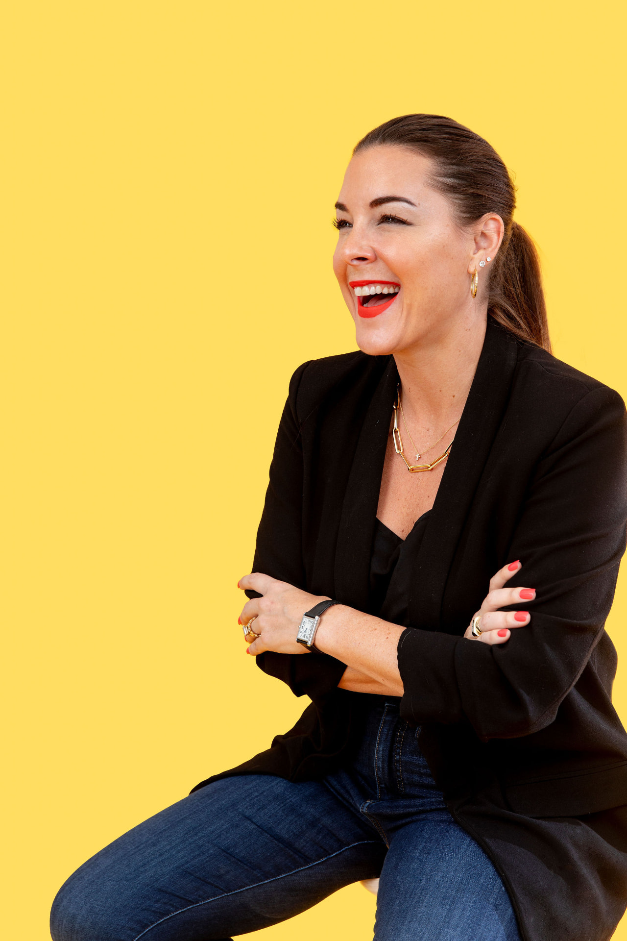 Ann Lopez laughing, in a black blazer against a butter yellow backdrop