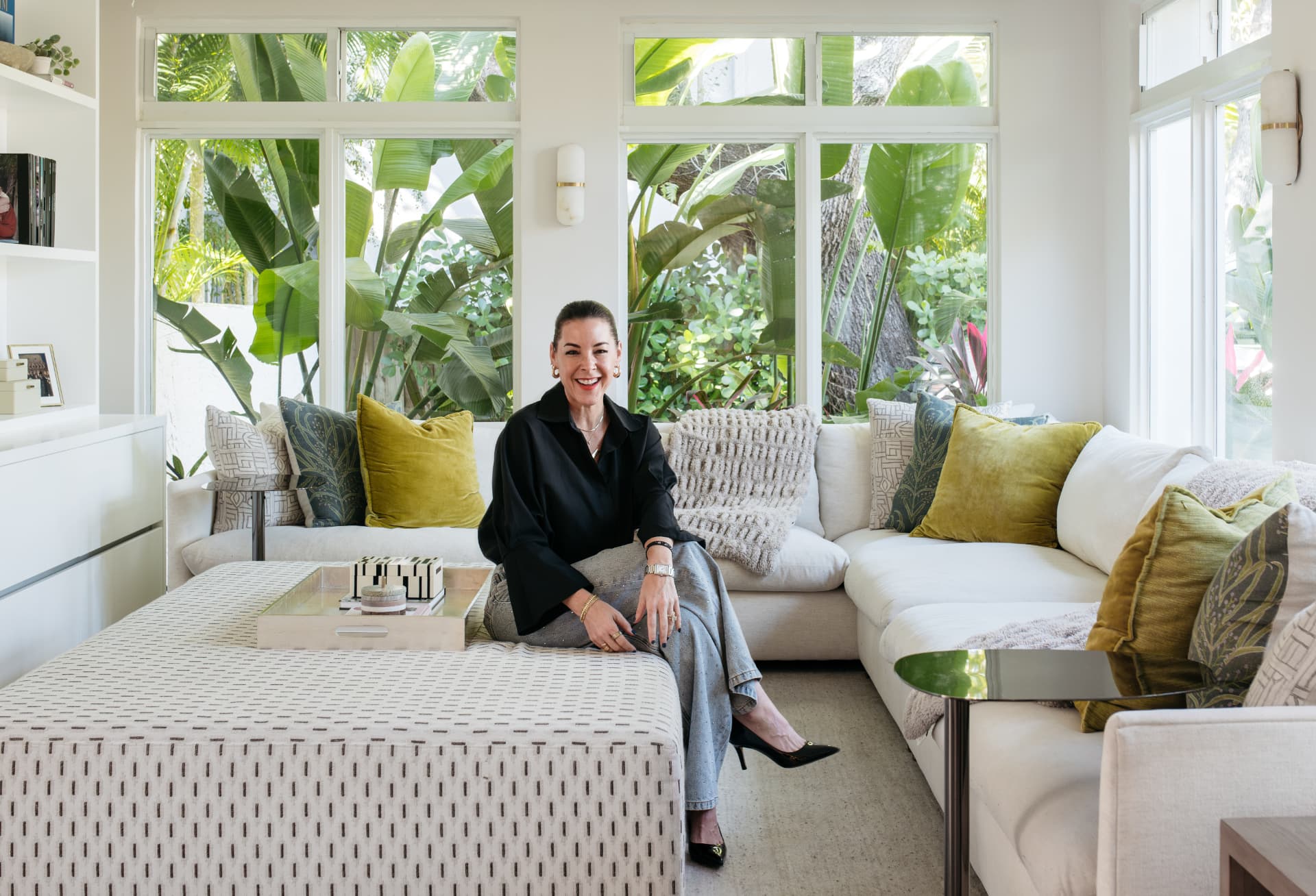Ann Lopez laughing on her sofa, framed by windows and palms